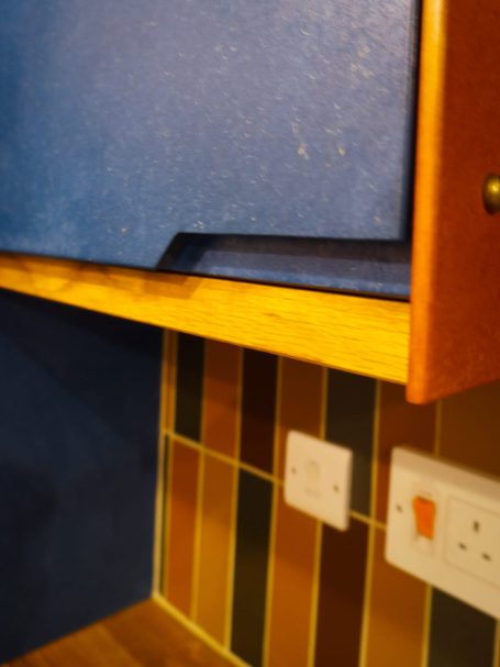 Blue kitchen cabinet edge above colourful tiled wall with electrical sockets.