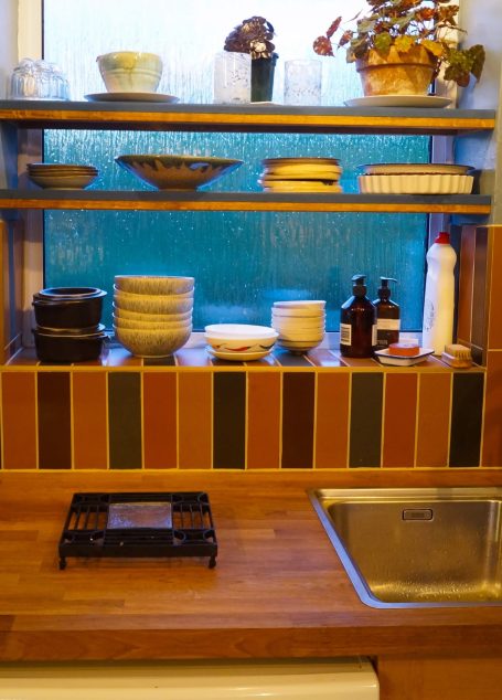 Kitchen shelf with various bowls, bottles, and a sink underneath.