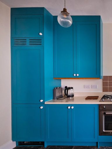 Bright blue kitchen cabinets with a white countertop and appliances.