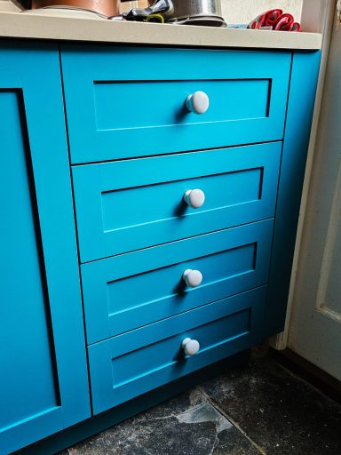 Bright blue kitchen cabinet with four drawers and white knobs.