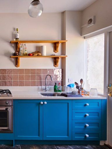 Modern kitchen featuring blue cabinetry, wooden shelves, and a sleek countertop with utensils.