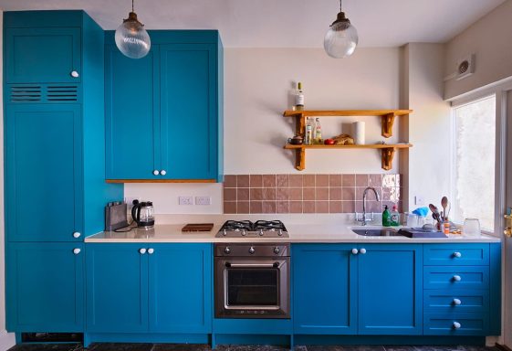 Modern kitchen with blue cabinets, wooden shelves, and stainless steel appliances.