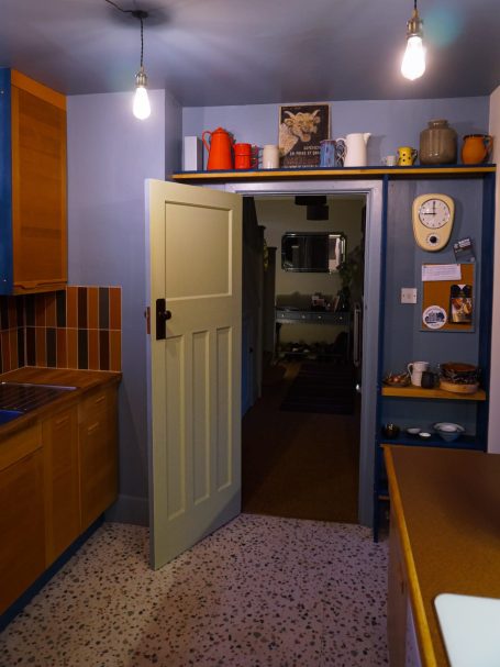 A doorway leads to a dimly lit room, with wooden cabinets and minimalist decor.