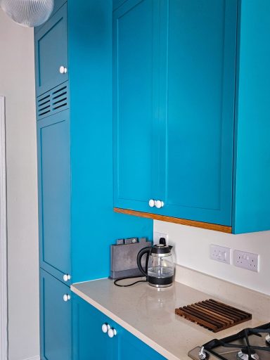 Bright blue kitchen cabinets with a kettle and countertop appliances on a light surface.