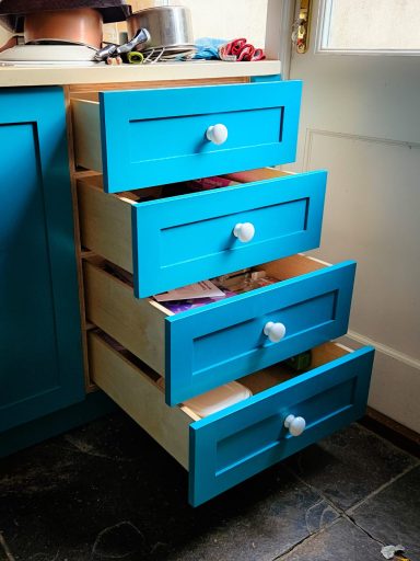 Turquoise kitchen drawers partially open, revealing various items inside.