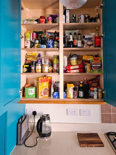 Well-organised kitchen cupboard filled with various jars, cans, and boxes of food.